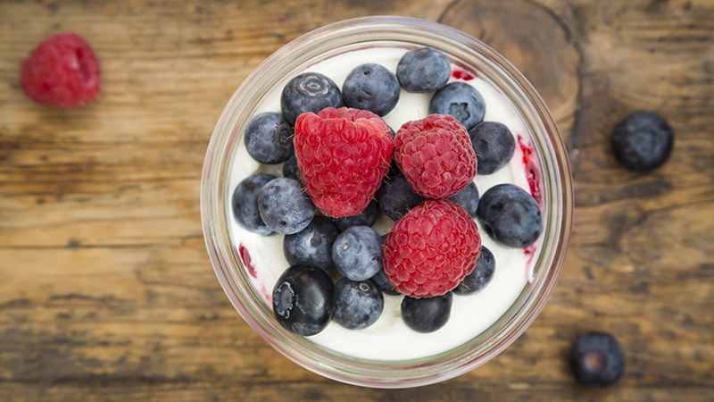 Glass of yogurt with fresh blueberries and raspberries on a wooden board.