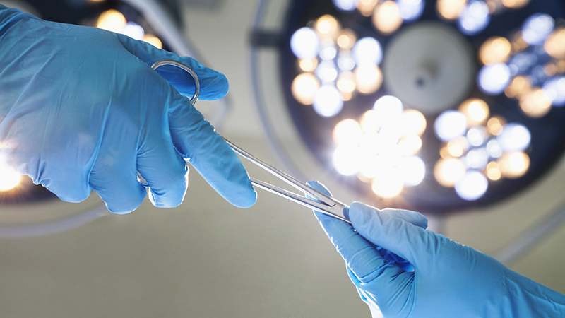 Closeup of gloved hands passing surgical scissors in an operating room. 