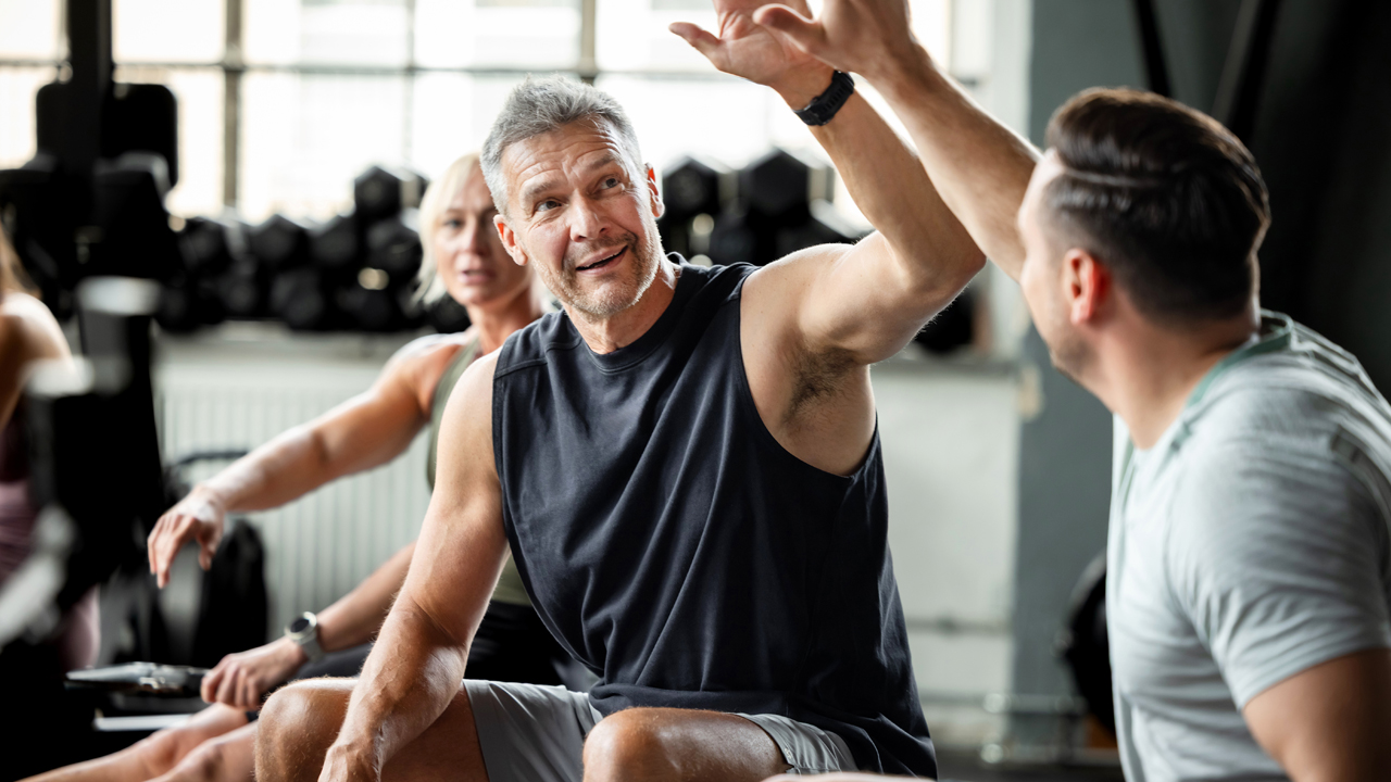 Two men in a gym celebrating their weight-training workout with a high five.