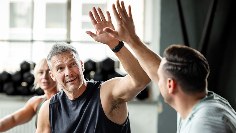 Two men in a gym celebrating their weight-training workout with a high five.