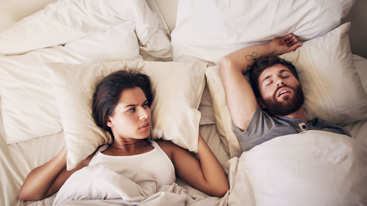 woman covers her ears with pillow while husband snores