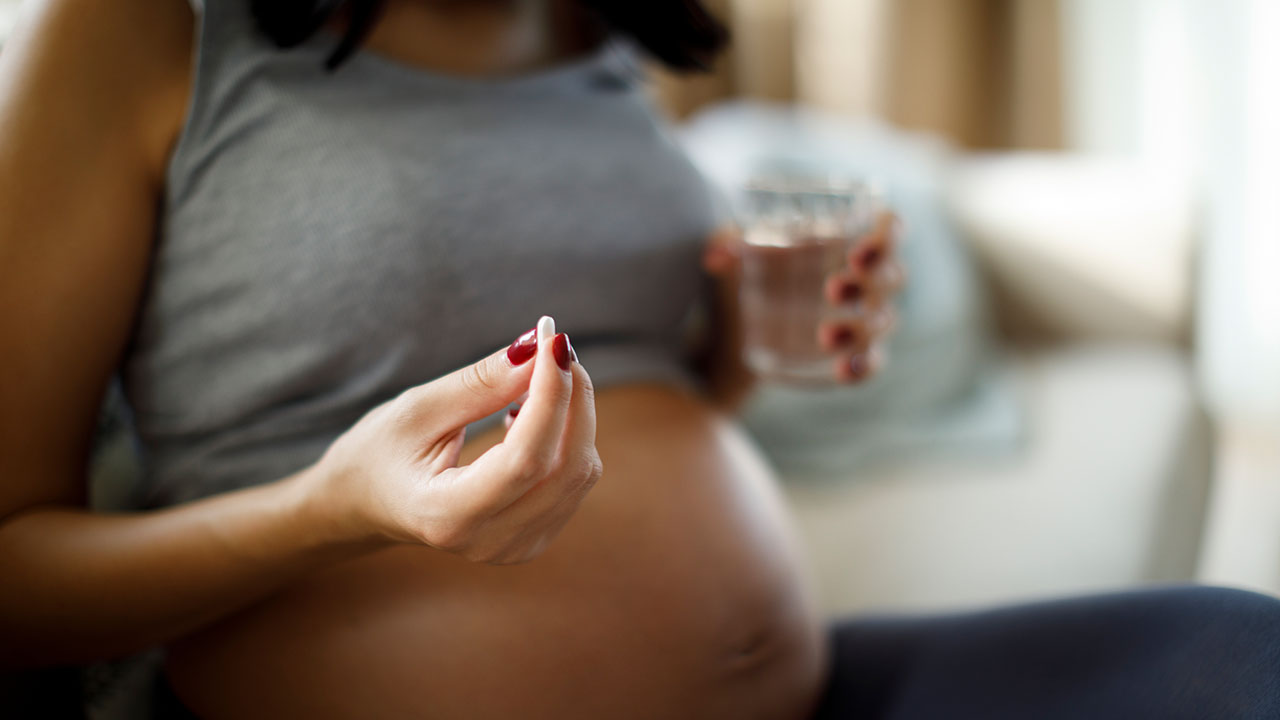 Pregnant woman holds vitamin and glass of water