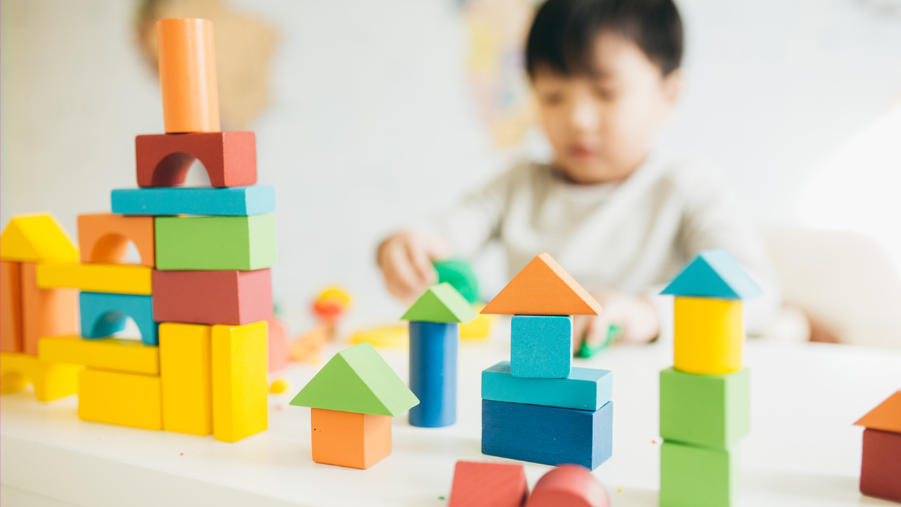 A child plays with multi colored wooden blocks in the foreground.