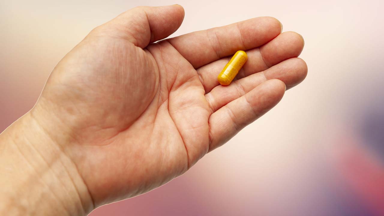A hand holding a golden turmeric pill.