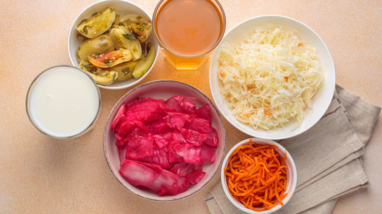 Six fermented foods, including pickled carrots, kefir and sauerkraut in bowls.