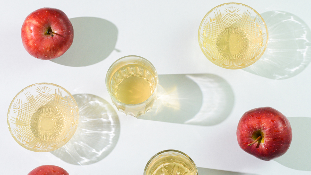 Apple cider vinegar and whole, red apples arranged on a light green table.