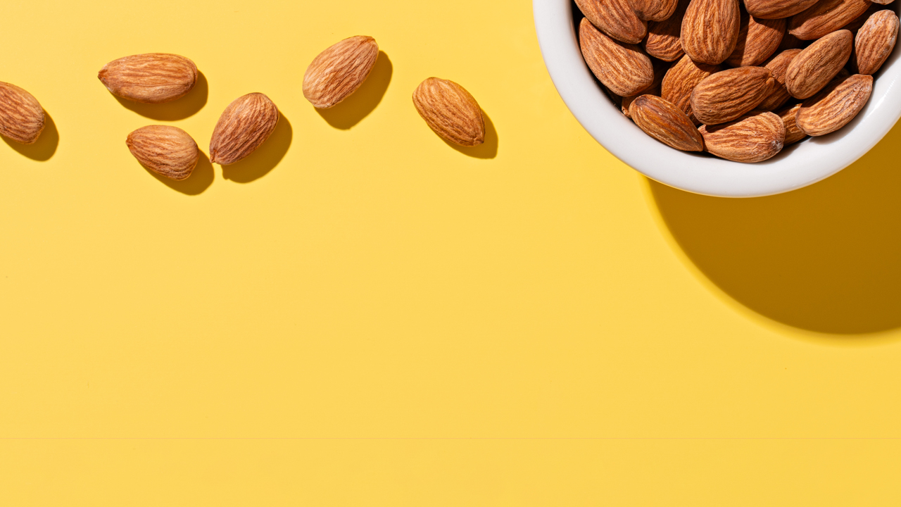 Almonds in a white bowl with a yellow background.