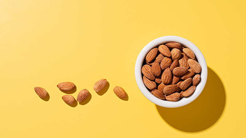 Almonds in a white bowl with a yellow background.