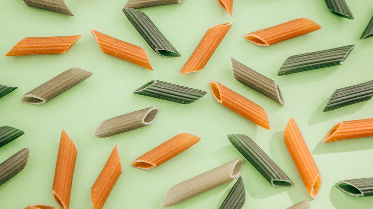 Green and orange penne pasta noodles arranged on a green background.