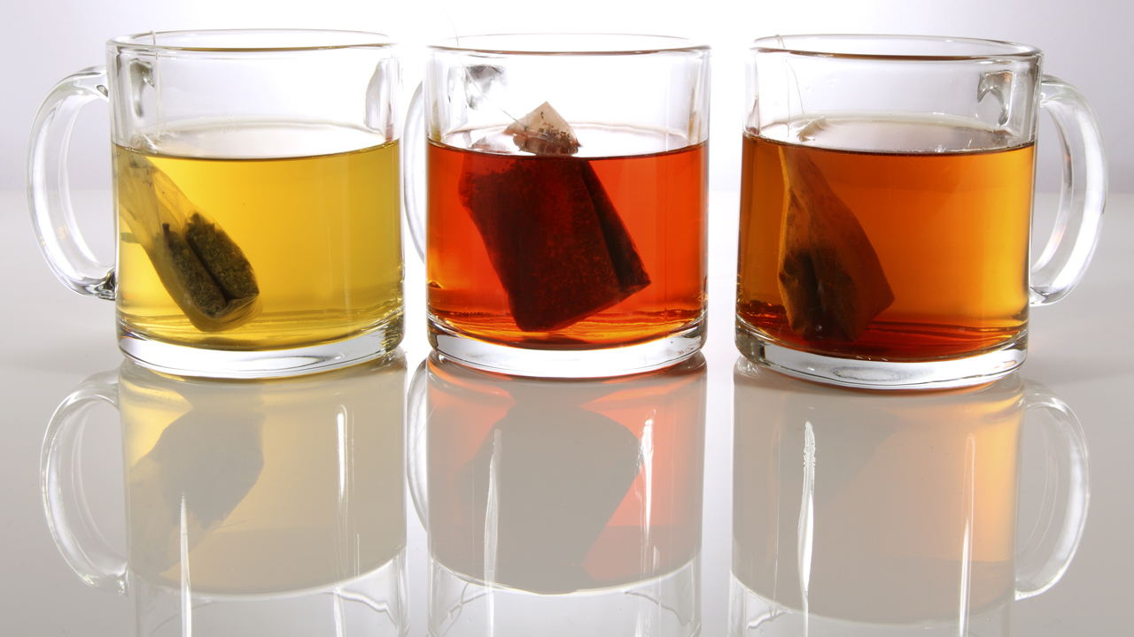 Three glass mugs of different types of tea on a table. 