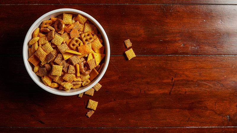 A bowl of Chex mix on a wooden table seen from above.