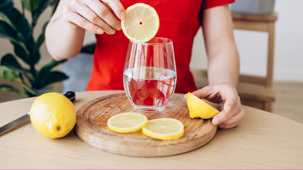 Person placing a slice of lemon into a glass water.