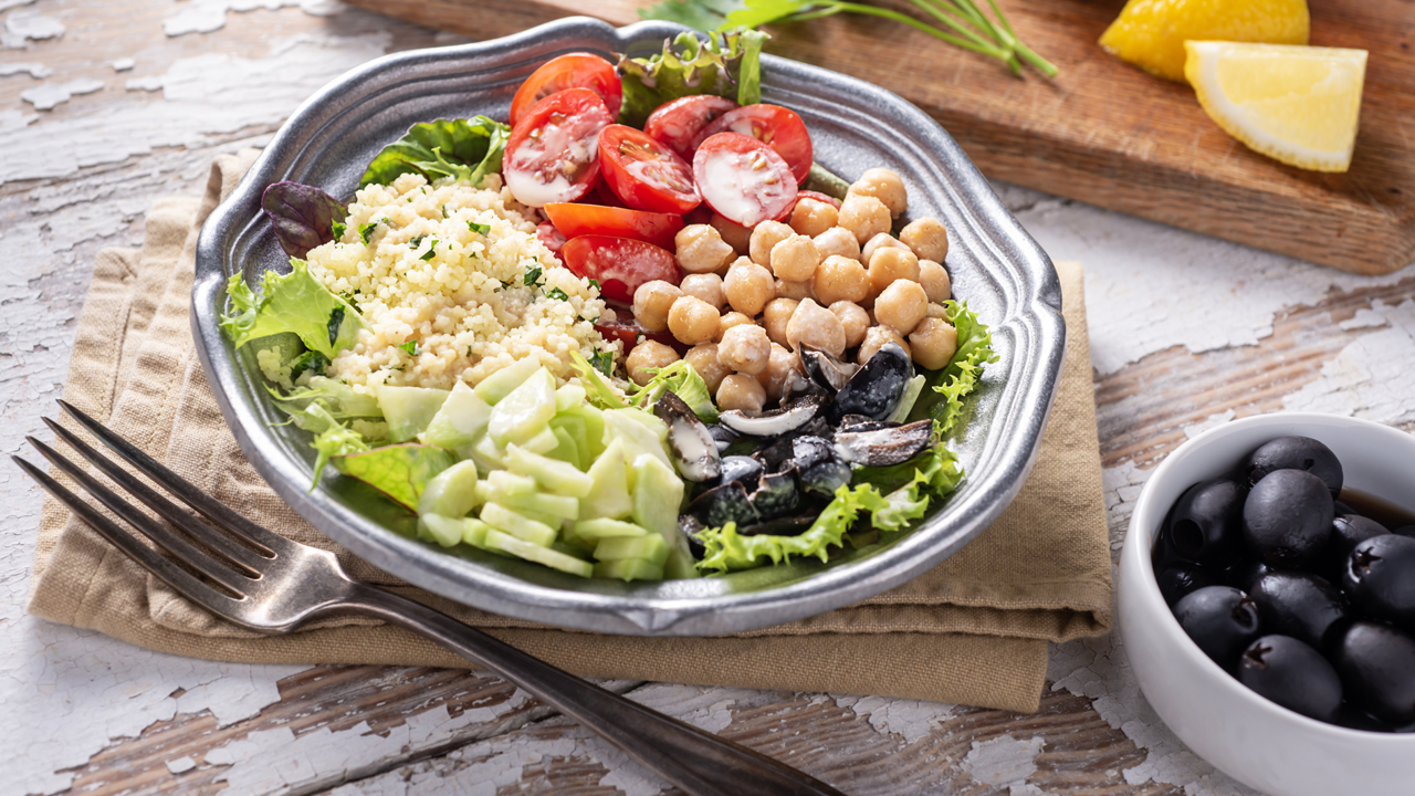 Salad, cucumbers, chickpeas, tomatoes, couscous, black olives, lemon and parsley representing the Mediterranean diet.