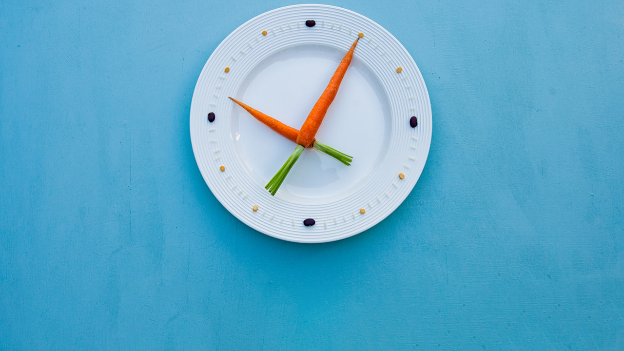 Clock made with two carrots as hands on a white plate, with rice and seeds for numbers.