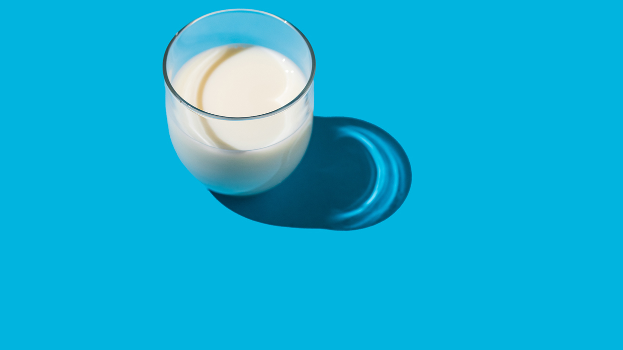Glass of milk in hard light on a blue background.