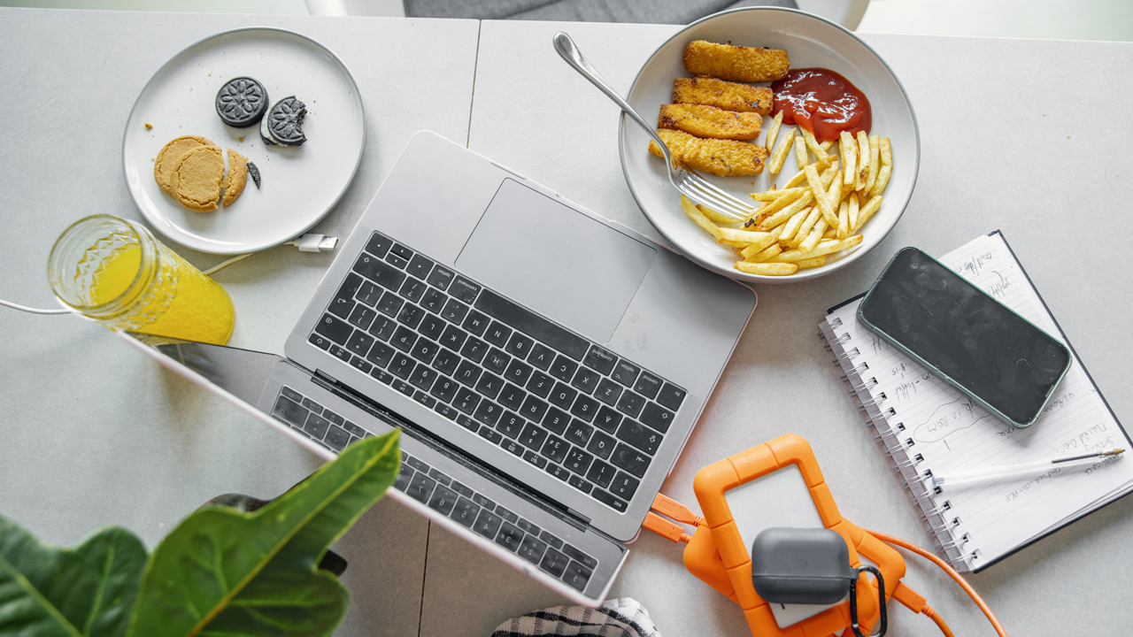 Ultra-processed foods on two plates, including cookies and French fries, fish sticks and ketchup with a glass of orange juice at a desk workstation