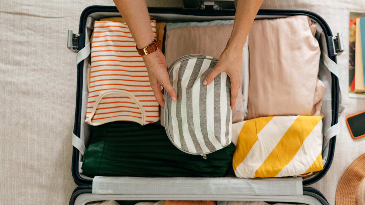 Person placing an item in an open suitcase.