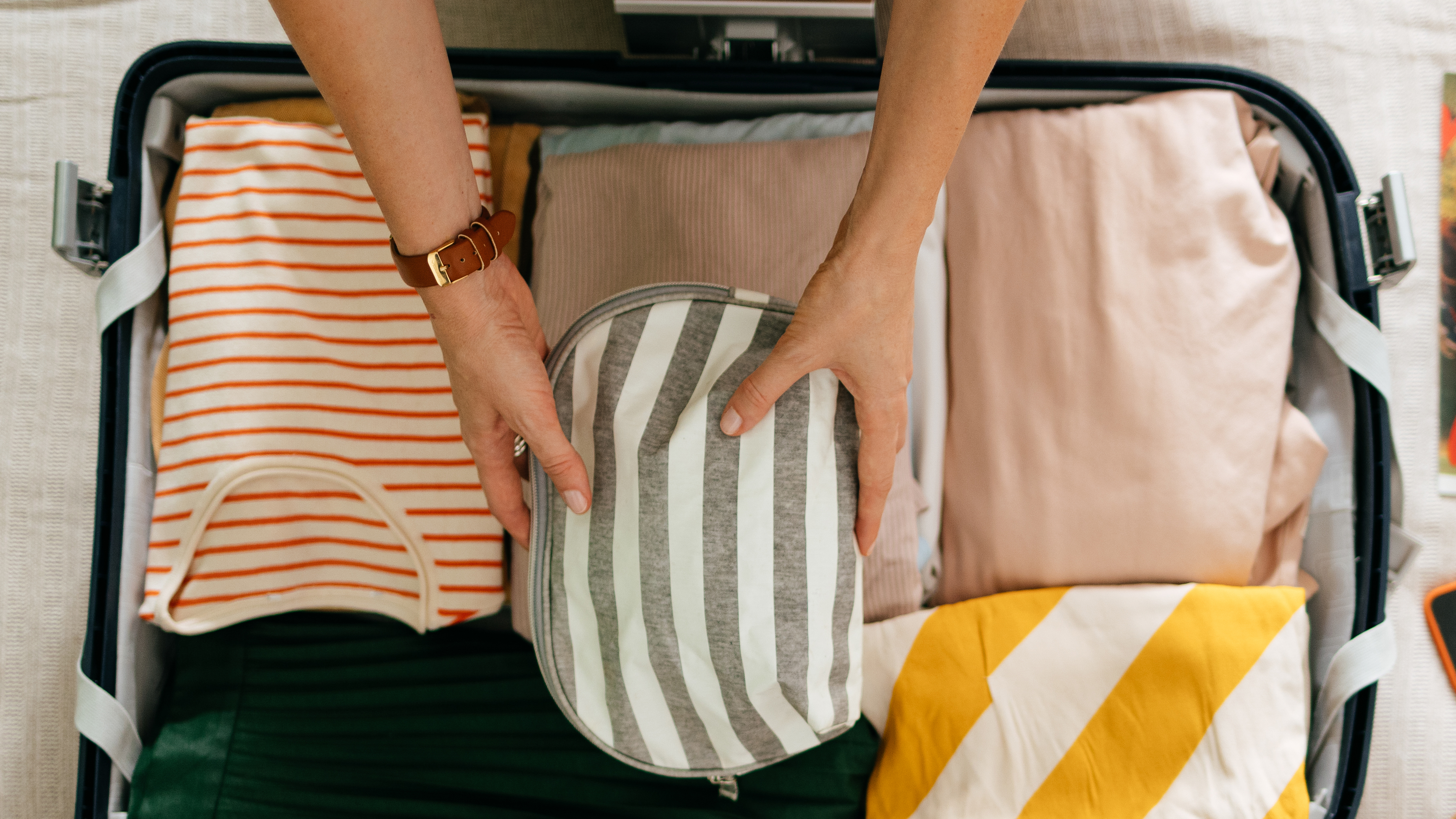 Person placing an item in an open suitcase.