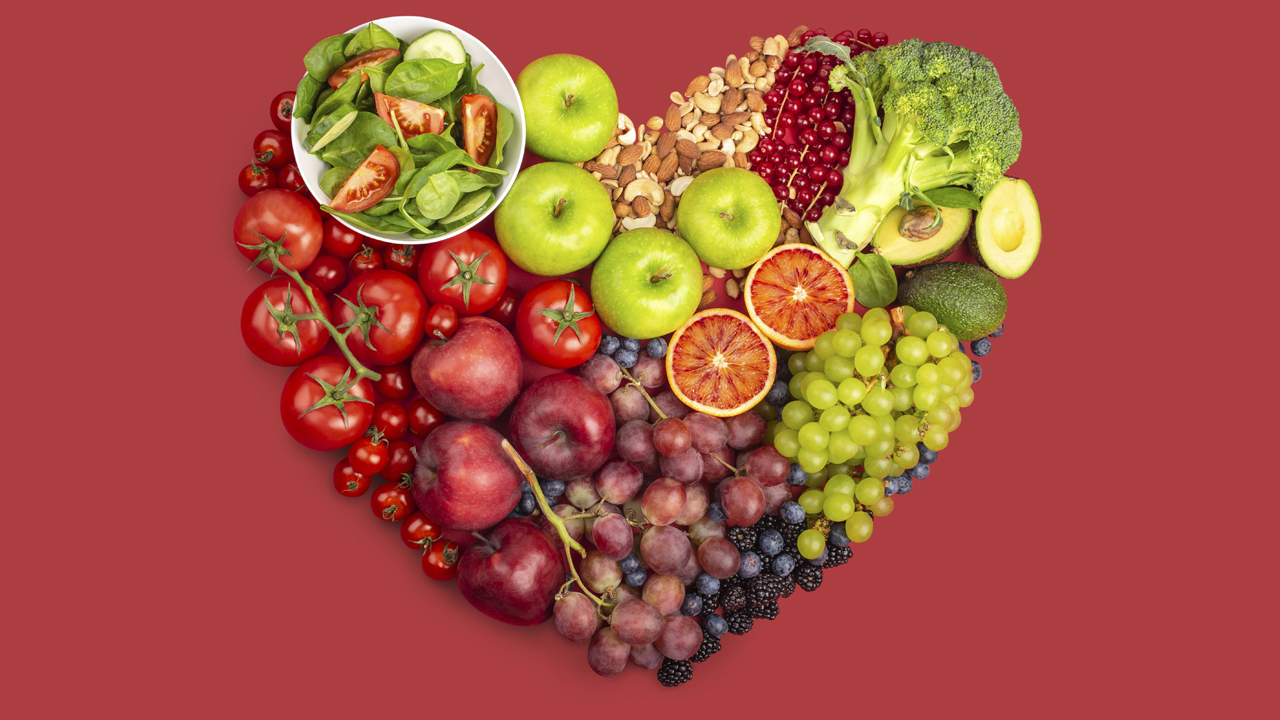 Several fruits, vegetables and nuts in the shape of a heart on a red background, representing healthy eating for heart health.