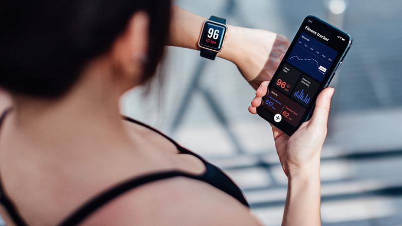 A view of a woman's wrist fitness tracker and phone. The fitness tracker shows"96" heartrate.