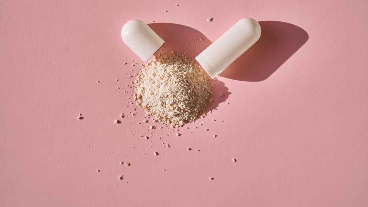 An open capsule with its contents on a pink background.