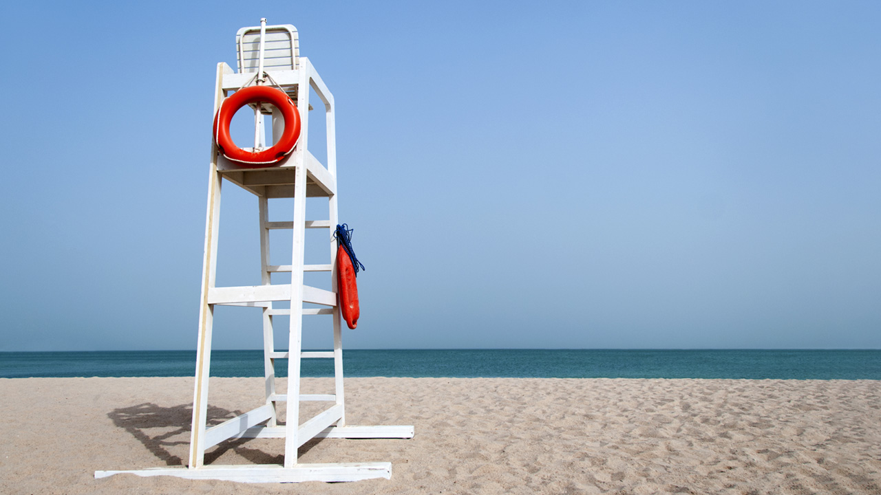 White life guard tower with a red life ring on a beach.