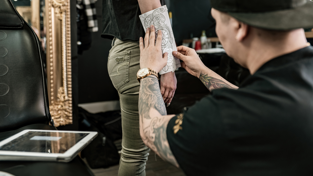 Tattoo artist placing a paper stencil with the tattoo design on a client’s leg.