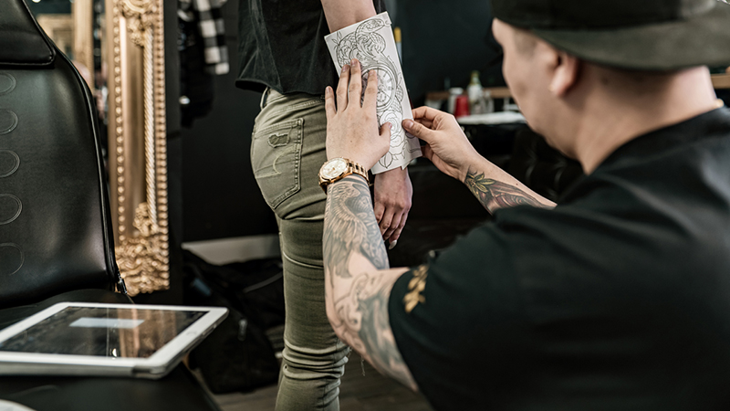 Tattoo artist placing a paper stencil with the tattoo design on a client’s leg.