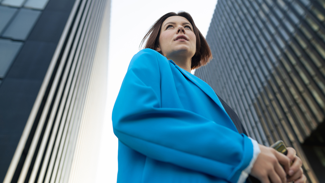 Business person wearing a blue blazer standing between two large office buildings.