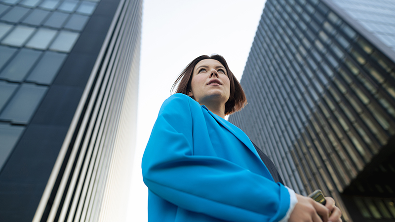 Business person wearing a blue blazer standing between two large office buildings.
