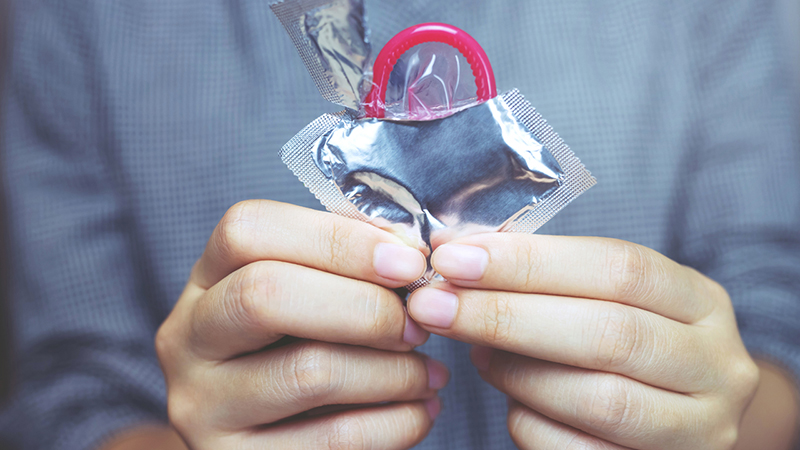 Person holding a half-unwrapped condom package with a pink condom sticking out of the wrapper. 