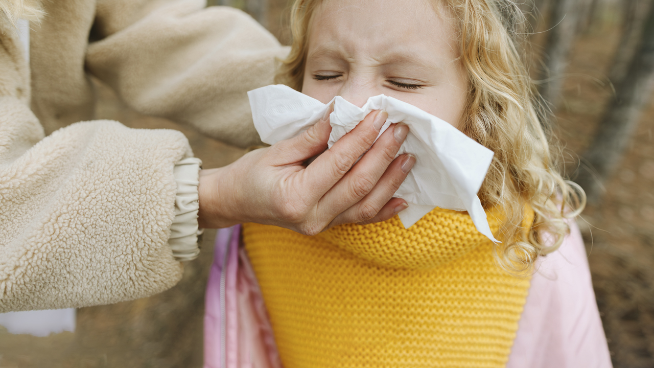 Woman wiping a little girl’s nose with a tissue.