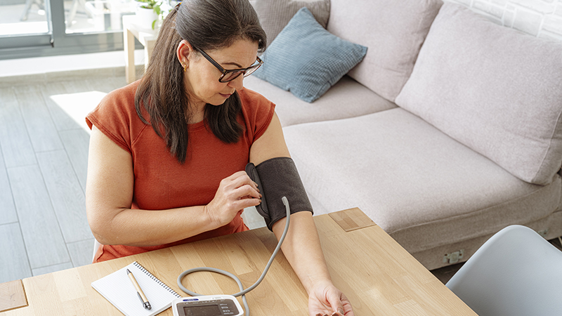 An adult taking an at-home blood pressure test on a kitchen table at home.