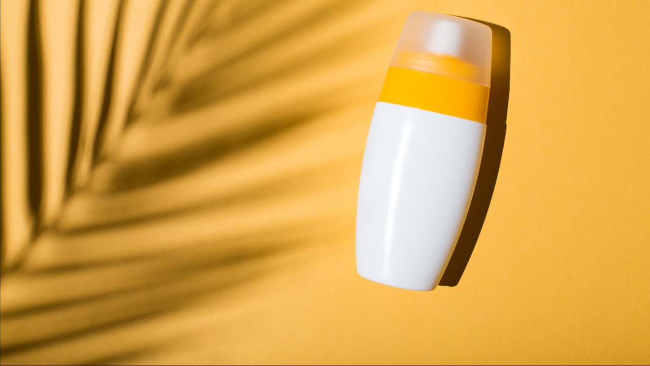 White bottle of sunscreen on a yellow background with a palm leaf shadow over it.