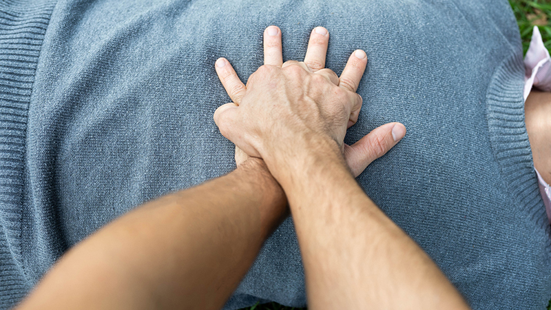 Hands crossed pressing down on chest of person lying on the ground, giving CPR.