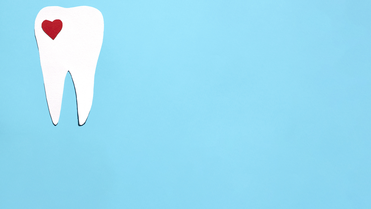 Cut paper illustration of a white tooth with a tiny red heart in the corner, on a blue background.