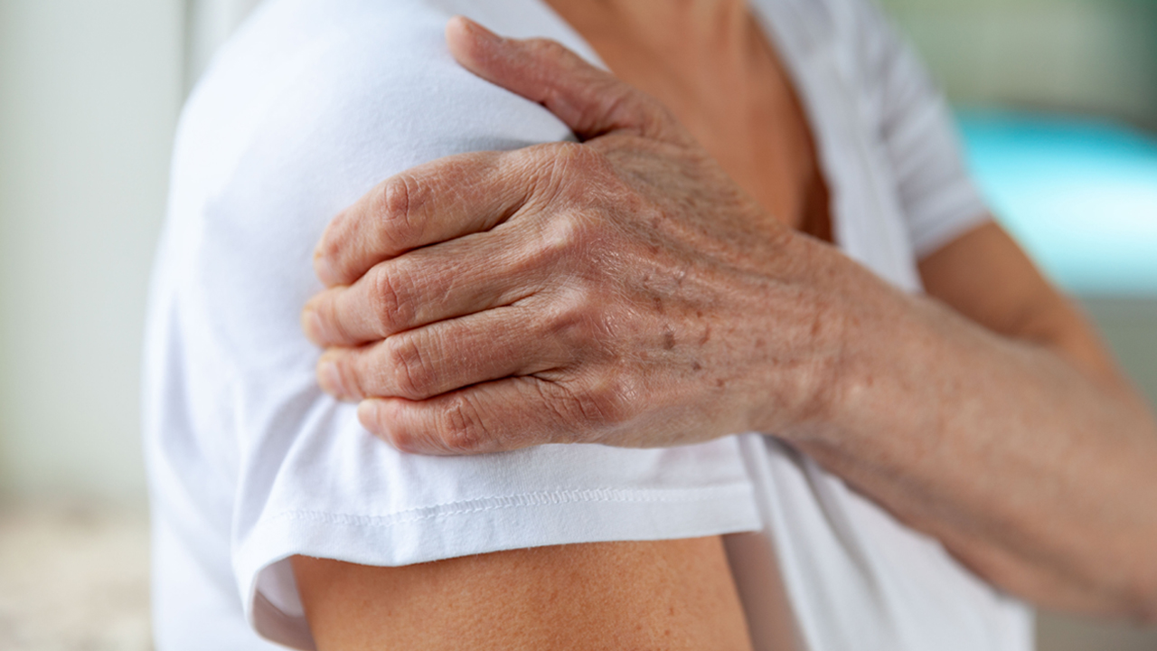 Mature person holding their shoulder as if in pain.