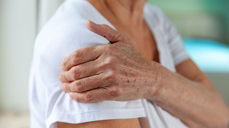 Mature person holding their shoulder as if in pain.