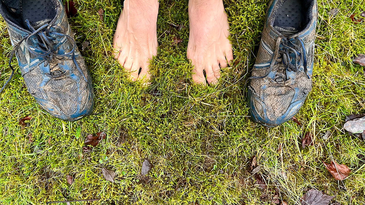 Feet on moss and grass next to running shoes.