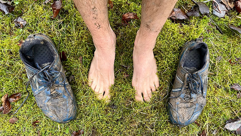 Feet on moss and grass next to running shoes.