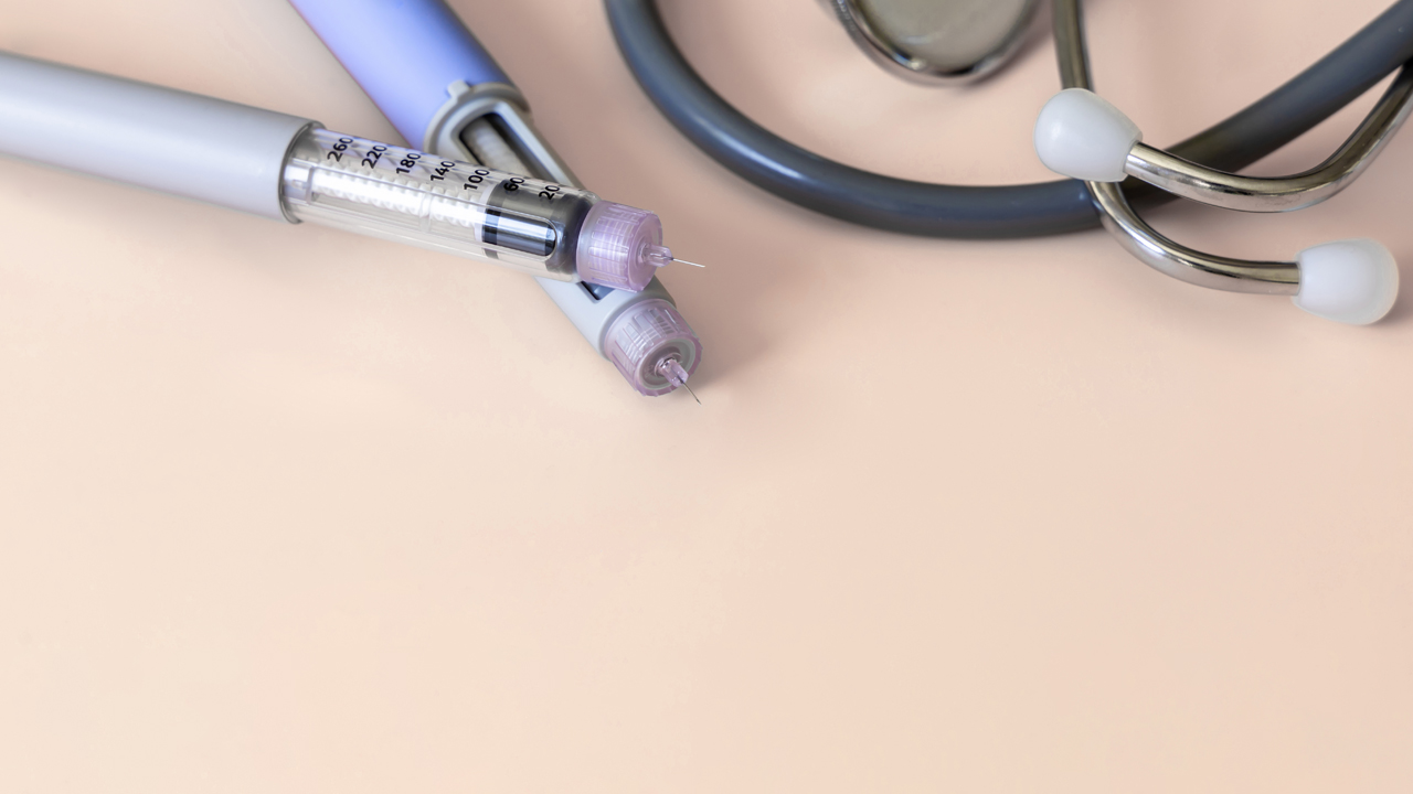 Two insulin injection pens on a table next to a stethoscope.
