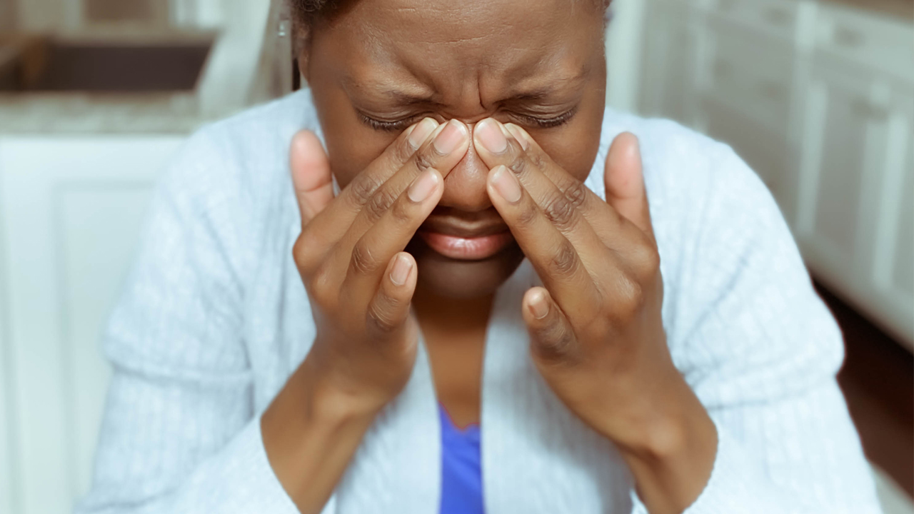 A person with medium toned skin holds the bridge of their nose in pain.