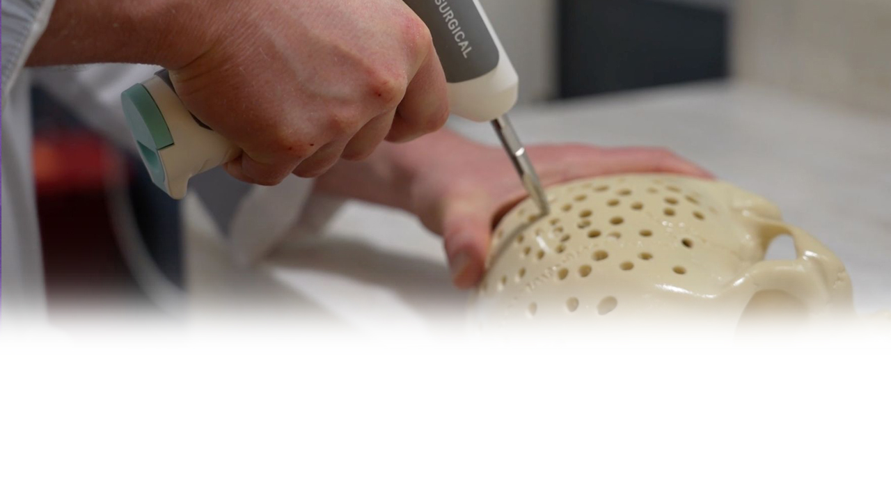 A hand using a drill on a plastic skull.