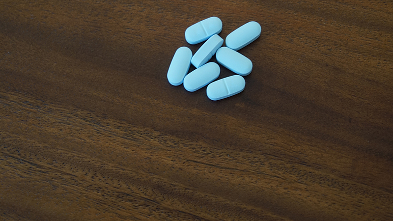 Seven light blue oblong pills in a group on a brown wooden table top.