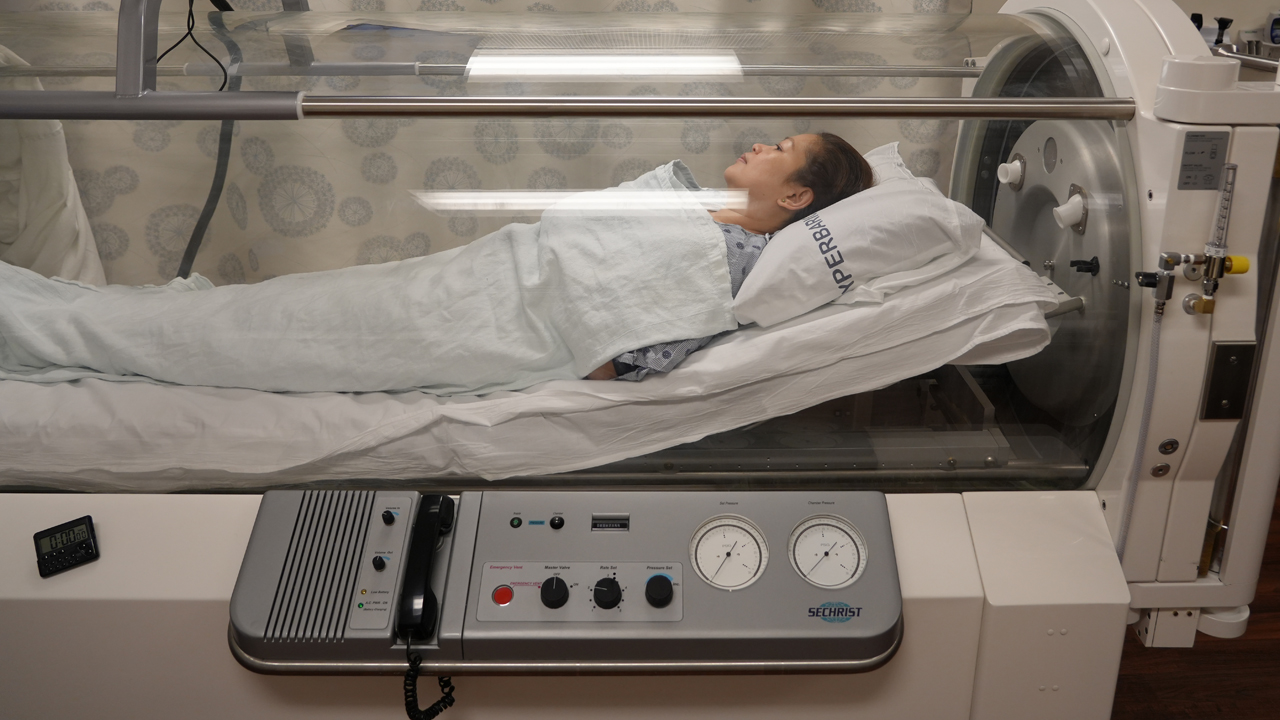 A patient is inside a hyperbaric oxygen chamber getting hyperbaric oxygen therapy to treat ulcerative colitis. 