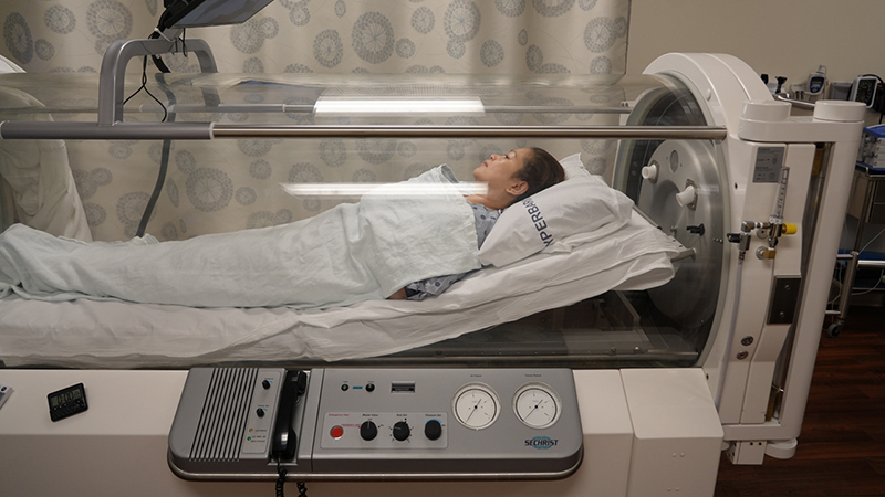A patient is inside a hyperbaric oxygen chamber getting hyperbaric oxygen therapy to treat ulcerative colitis. 