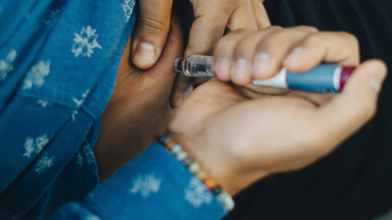 Person injecting their abdomen with a blue and white syringe.