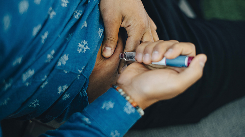 Person injecting their abdomen with a blue and white syringe.