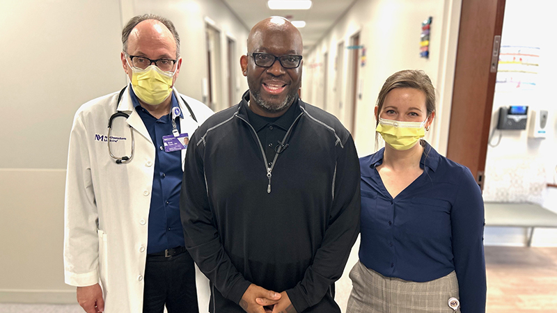 Art Gillespie in street clothes standing with his physician and nurse in a hospital corridor.
