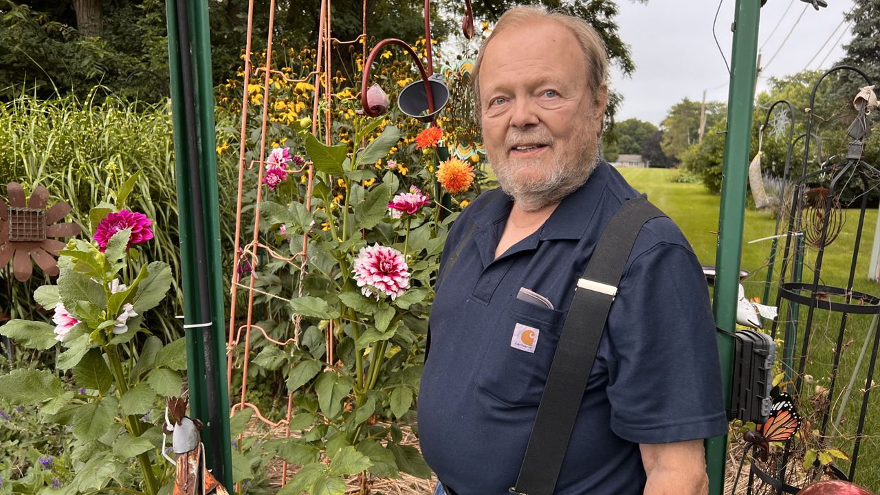 Harry Piehl stands smiling as his dahlias bloom in his garden. 